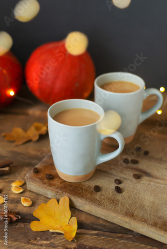 Two flavored pumpkin coffee with spices in ceramic cups on a wooden table with orange pumpkins in the background. Bokeh. Autumn mood. Time to drink hot beverage.