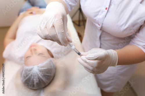 The cosmetologist holds the filler for injections of hyaluronic acid and removes the protective cap from the needle