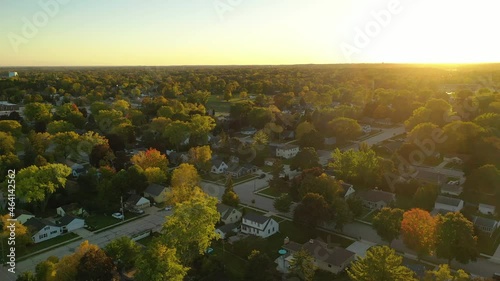 Sunset highlights autumn neighborhood scene with homes and colorful trees along the street, aerial drone shot