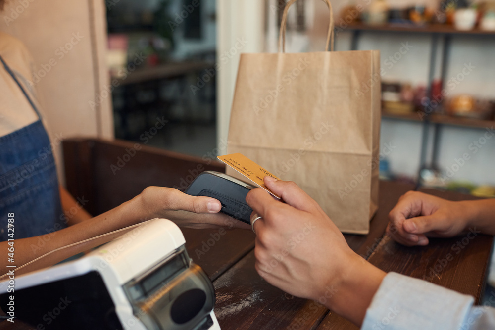 Obraz premium Close-up of unrecognizable customer paying with wireless card and putting it to terminal in shop of handmade goods