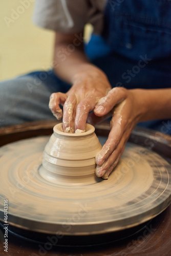 Close-up of unrecognizable potter with wet dirty hand molding walls of clay pot on pottery wheel