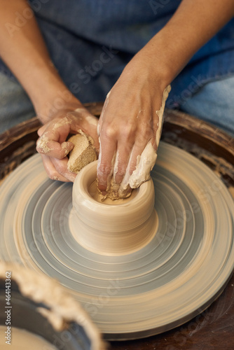 Close-up of unrecognizable potter working with clay on pottery wheel and removing water stains from pot with sponge
