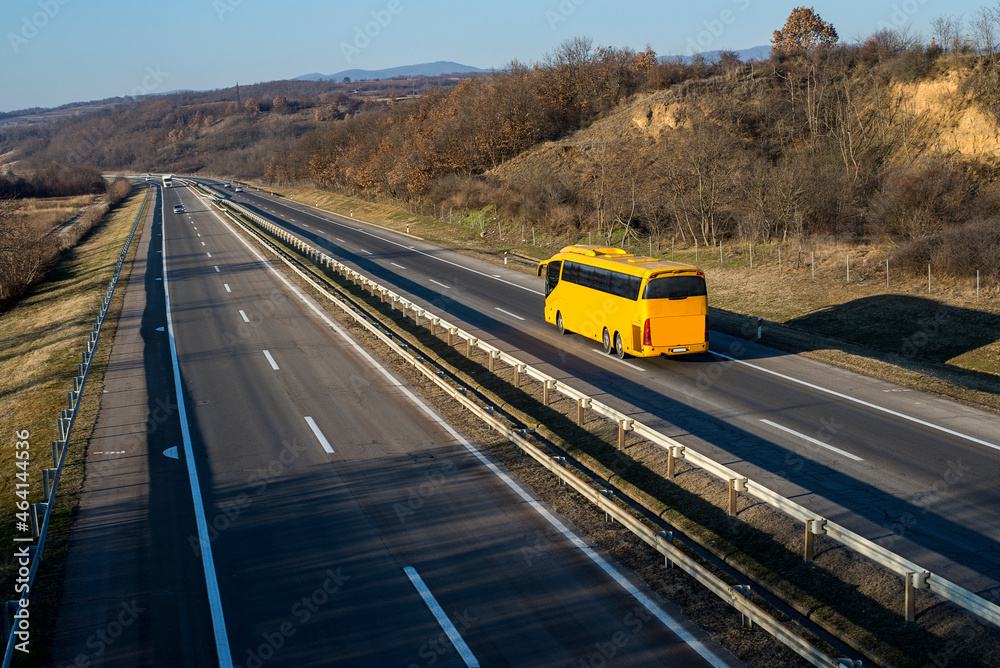 Yellow bus driving on asphalt road in a rural landscape.