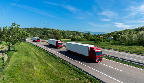Convoy of Big Transportation trucks departing on a country highway under a blue sky. Business Transportation And Trucking Industry.	