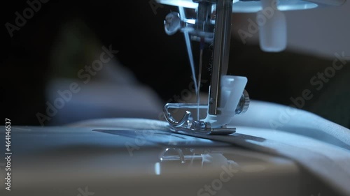 Needle for sewing machine in motion. The close-up of the sewing machine needle quickly moves up and down. The seamstress sews gray fabric in the sewing workshop. The process of sewing the fabric.	