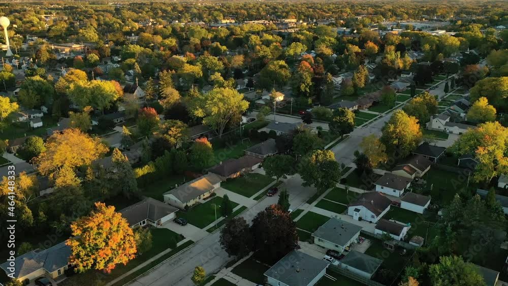 Sunset autumn neighborhood scene with homes and colorful trees, car driving down the street, aerial drone shot