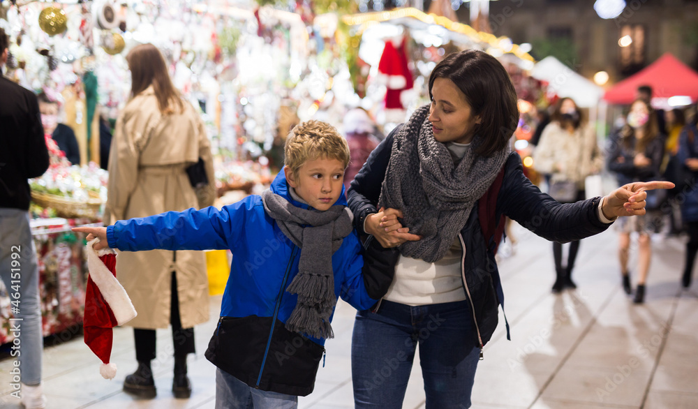 Portrait of happy woman visiting traditional city Christmas fair with her preteen son, walking among shopping stalls