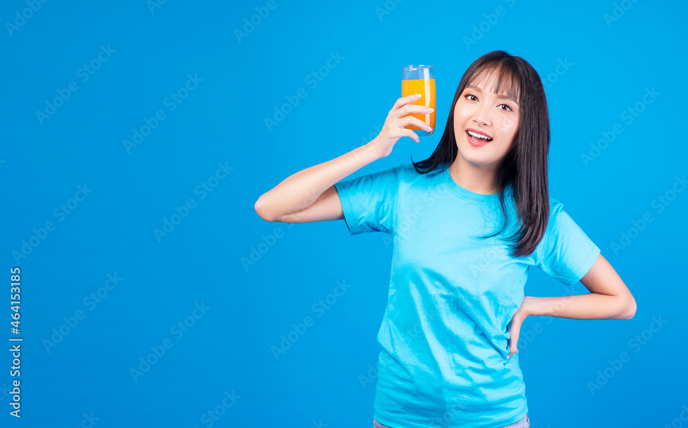 Healthy fruit vitamin beverage concept. Enjoy leisure young woman wear casual holding glass with fresh organic orange juicy in own hands while standing feeling relax over isolate blue background. Healthy fruit vitamin beverage concept. Enjoy leisure young woman wear casual holding glass with fresh organic orange juicy in own hands while standing feeling relax over isolate blue background.