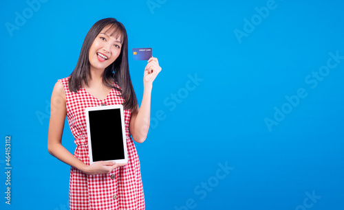 Financial payment online shopping and money transfer concept. Excited smile young woman holding digital tablet and mockup credit card for internet banking while standing over isolated blue background.