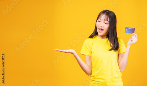 Payment purchase and financial concept. Cheerful young woman wearing casual clothes while holding credit card mockup in own hand while standing with copy space over isolated yellow background.