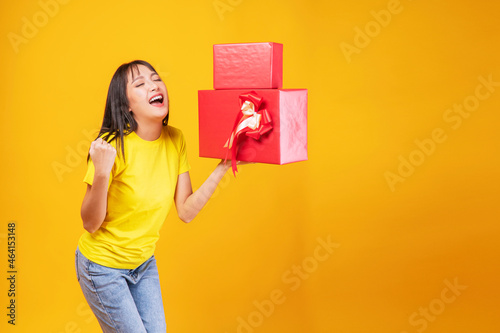 Surprise greeting anniversary birthday or celebration christmas and new year. Cheerful excited young woman holding two red and gold gift box in own hand while standing over isolated yellow background.
