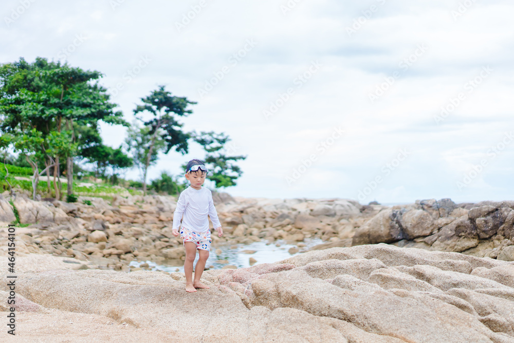 4 years old asian boy play on the rock on sea beach.Vacation and relax.Playful active kid on beach in summer vacation and child development.Asian kid toddler boy play in sea sand beach in thailand. 4 years old asian boy play on the rock on sea beach.Vacation and relax.Playful active kid on beach in summer vacation and child development.Asian kid toddler boy play in sea sand beach in thailand.
