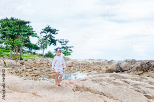 4 years old asian boy play on the rock on sea beach.Vacation and relax.Playful active kid on beach in summer vacation and child development.Asian kid toddler boy play in sea sand beach in thailand. © MIA Studio