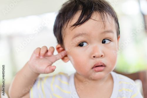 Little asian toddler baby boy has earache when insects inside outdoor baby infant boy hands touching in ear and pain.deaf kid.Flu and sick.Clean up earwax.Accident in kid with ear.Condition and clean. photo