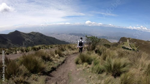 A woman is wearing a black backpack and a black cap while walking on a trail of Rucu Pichincha, on the moorlands of the Andes in Ecuador.