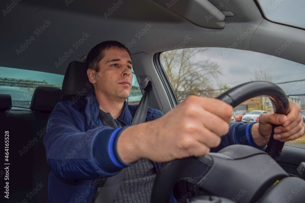 A young man in a blue jacket with a seat belt is driving a car