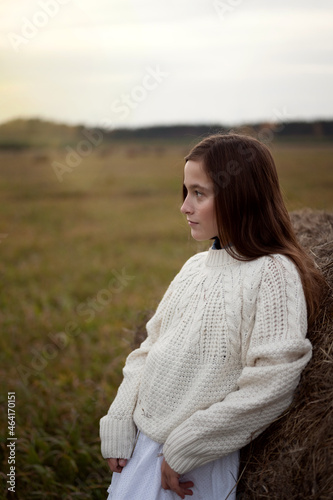 a teenage girl walks in a field with haystacks