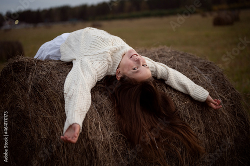 a teenage girl walks in a field with haystacks