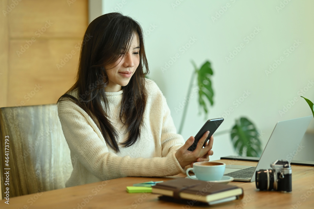 Young woman sitting in front of laptop computer and checking social media on her smart phone. Young woman sitting in front of laptop computer and checking social media on her smart phone.