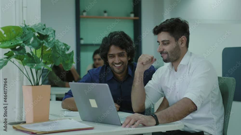 Two young Indian man happy and smiling friends are watching and enjoying video or movie together using laptop on office.Smiling and discussing about project on laptop in a start up business firm. Two young Indian man happy and smiling friends are watching and enjoying video or movie together using laptop on office.Smiling and discussing about project on laptop in a start up business firm.
