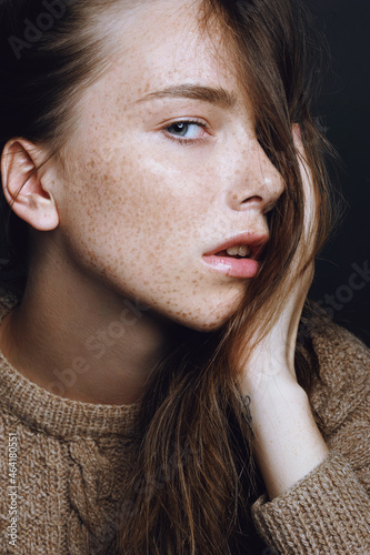 Young beautiful girl with freckles face in cozy knitted autumn sweater touching her face