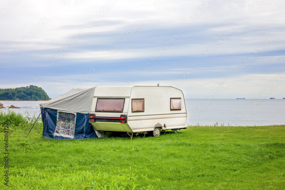 Trailer motor home and a tent on the grassy part of the beach at sunset. Leisure mobile camping home for tourists overlooking the blue sea and cape. Adventure relaxing travel on caravan van Trailer motor home and a tent on the grassy part of the beach at sunset. Leisure mobile camping home for tourists overlooking the blue sea and cape. Adventure relaxing travel on caravan van