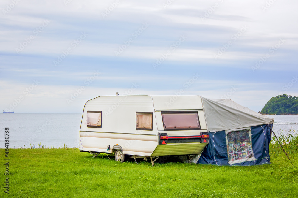 Trailer motor home and a tent on the grassy part of the beach at sunset. Leisure mobile camping home for tourists overlooking the blue sea and cape. Adventure relaxing travel on caravan van
