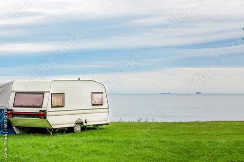 Trailer motor home and a tent on the grassy part of the beach at sunset. Leisure mobile camping home for tourists overlooking the blue sea and cape. Adventure relaxing travel on caravan van