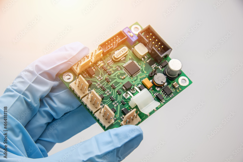 Hand in a blue glove holds pcb chip assembly on pcb backround on the production of printed circuit boards Hand in a blue glove holds pcb chip assembly on pcb backround on the production of printed circuit boards