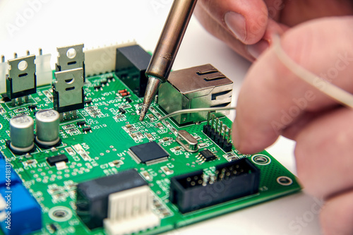 Male hands solder components onto a printed circuit board using copper and a soldering iron. Electronics repair. Selective focus. photo