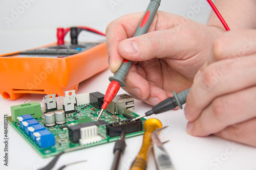 Male measures voltage with an ammeter on a printed circuit board. Electronics repair with tester. Selective focus.