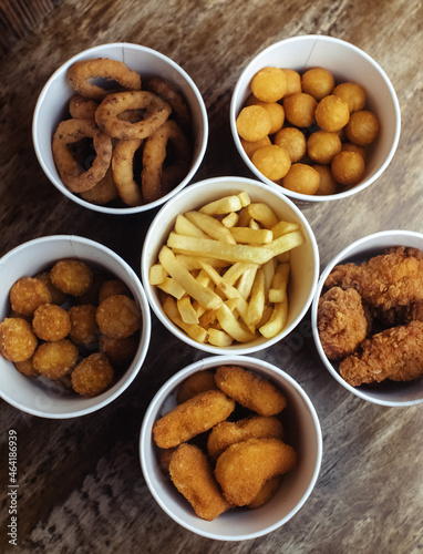 Top view of onion rings, cheese balls, chicken nuggets, wings in batter, fries and cheese sticks. Six-course set in paper buckets. Fast food cafes and restaurants. Food is laid out in shape of flower