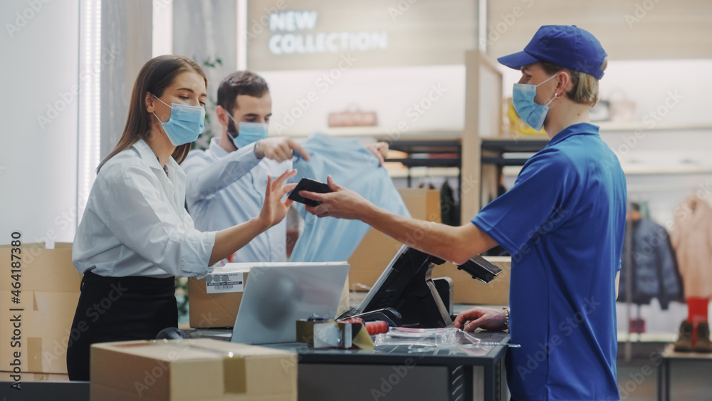 Clothing Store Checkout Cashier Counter: Female and Male Retail Sales Managers wearing Protective Face Masks Give Package to Online Order Delivery Person. Designer Brands Available on Internet - obrazy, fototapety, plakaty 