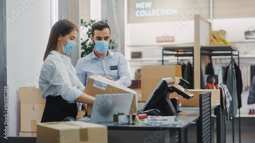 Clothing Store Checkout Cashier Counter: Female and Male Retail Sales Managers Wearing Protective Face Masks Packing Online Ordered Clothes. Fashion Shop with Merchandise Available on Internet
