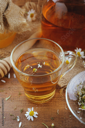 Glass of chamomile tea with honey and flowers on wooden table