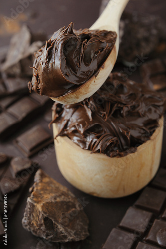 Chocolat butter in wooden bowl and dark chocolate chips, bar and chopped on brown background