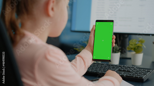Close up of child holding green screen on smartphone for homework and school tasks. Young girl looking at display with mockup template and isolated background for remote education.