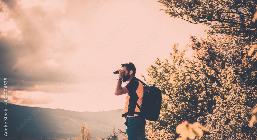 handsome man trekking in nature in autumn using binoculars slow travel