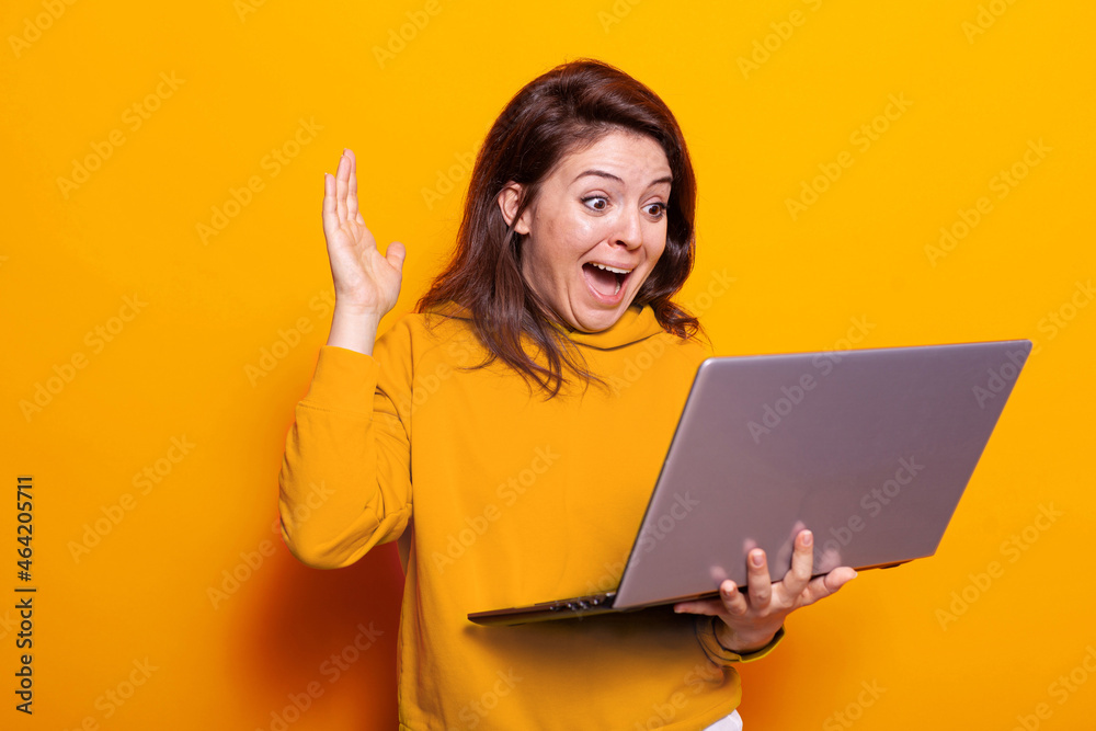 Smiling person waving hand at video call on laptop in studio. Young woman feeling excited and using online video conference while holding modern device with webcam. Remote conversation Smiling person waving hand at video call on laptop in studio. Young woman feeling excited and using online video conference while holding modern device with webcam. Remote conversation