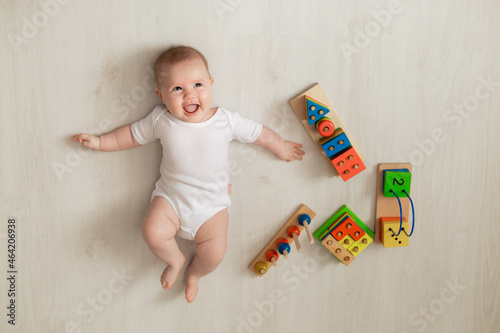 cheerful newborn baby in a white bodysuit lies on his back on the floor and plays with educational toys. products for children. concept of a happy childhood and motherhood. child care. space for text