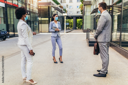 Three employers standing in social distance wearing face mask looking at each other and talking