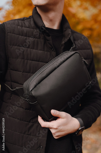 Closeup unrecognizable man holding black leather messenger bag in a autumn city