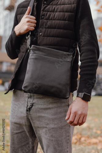 Closeup unrecognizable man holding black leather messenger bag in a city