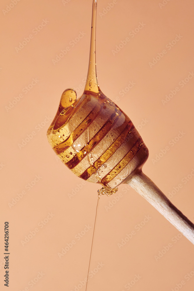 Obraz premium Minimalistic picture with Wooden dipper with honey falling down on brown background