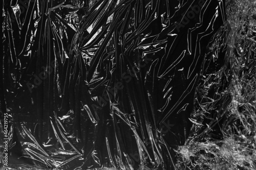 Reflecting light and shadow on creases and folds in scrunched plastic foil on black background