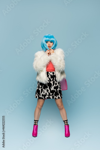 Full length of stylish asian woman in wig touching hair on blue background © LIGHTFIELD STUDIOS