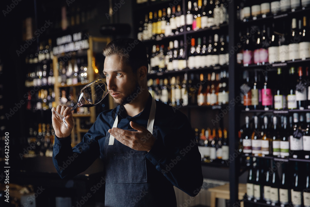 Winemaker sommelier man sniffing aroma red wine in glass background bottles restoran