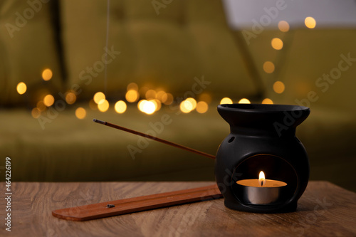 Black aroma lamp,candle flame and incense sticks against cozy warm lights on the home sofa.Empty space photo