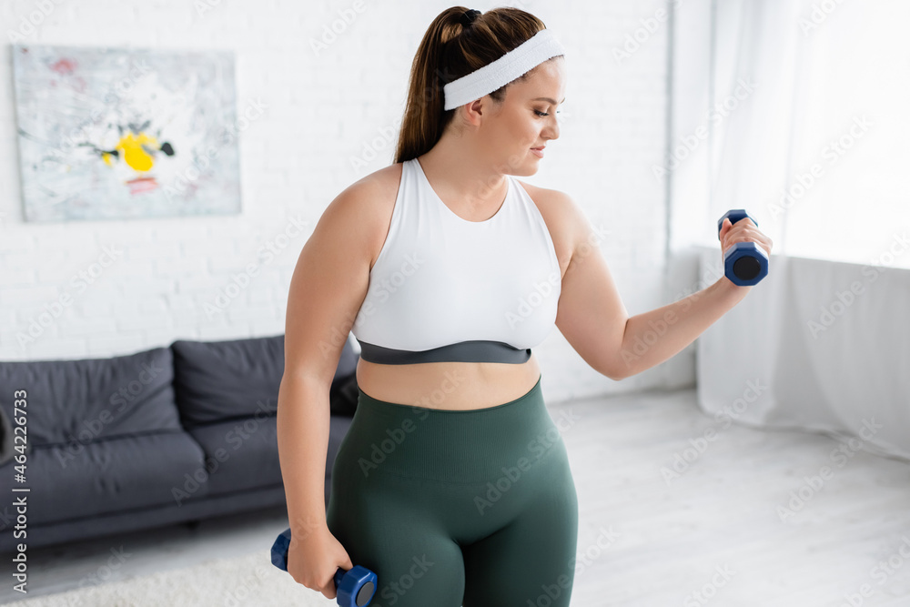 Side view of plus size woman training with dumbbells in living room