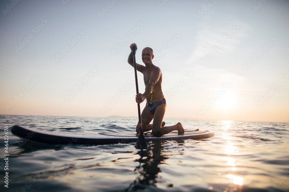 Senior man paddling board on a sunset sea	